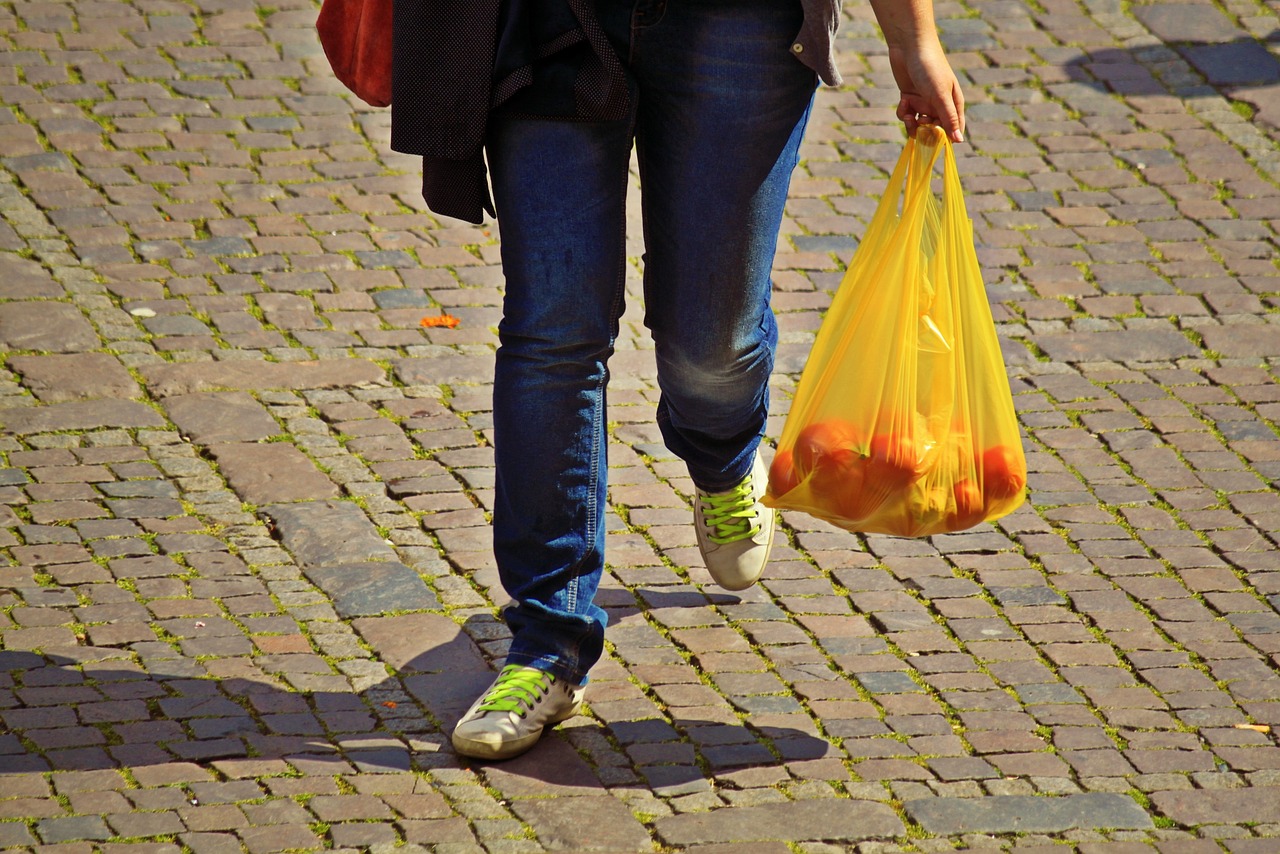 Person trägt einen gelben Plastikbeutel mit Obst