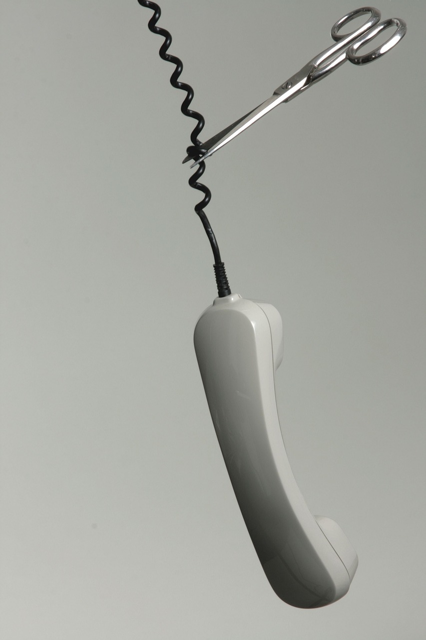 Hängender Telefonhörer am Spiralkabel mit angesetzter Schere am Kabel