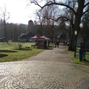 Blick auf die Trinkhalle und die Marktstände von Grobauer Leder und dahinter Korbmacherei Kreative Finger bei sonnigem Wetter auf dem Bauernmarkt März 2024