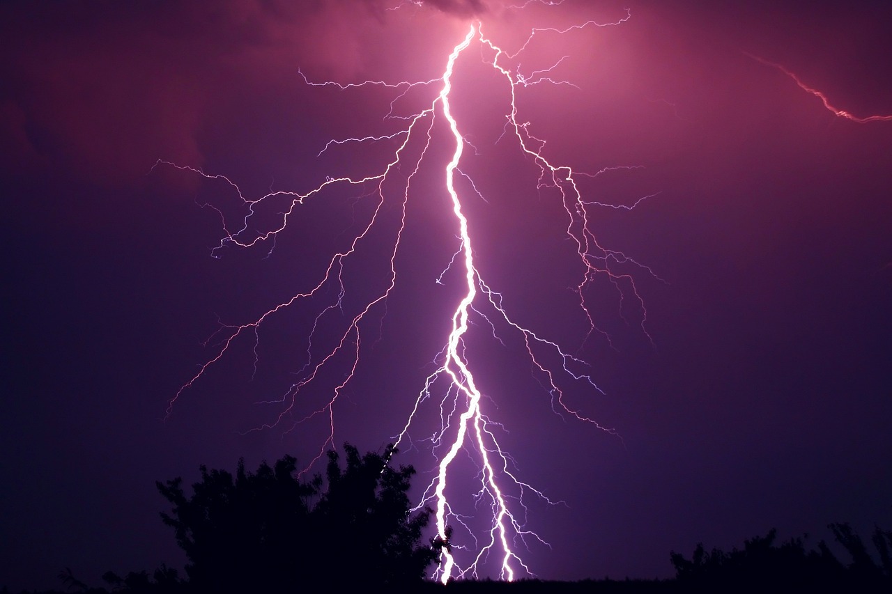 Blitz bei Gewitter mit schemenhaften Bäumen im Vordergrund