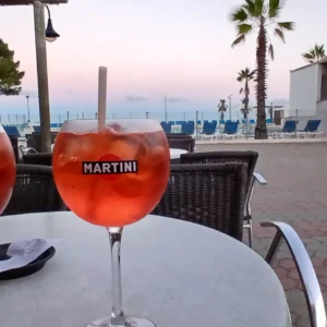 2 Gläser mit Aperol Spritz an einer Strandbar mit Blick auf den Pool und Strand.