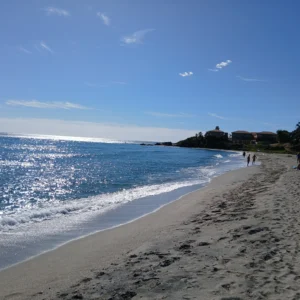 Strand mit feinem Sand und wenigen Menschen, die am Ufer entlanggehen, unter blauem Himmel mit wenigen Wolken auf Korsika.