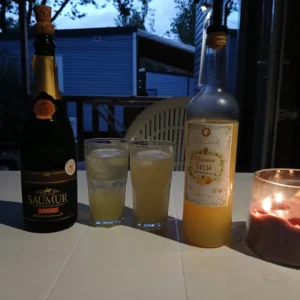 Zwei Gläser mit gelblichem Getränk, daneben Flaschen mit Etiketten, links 'Saumur', rechts 'Limon Cassis Artisanale', rechts brennende Kerze in Glasbehälter.