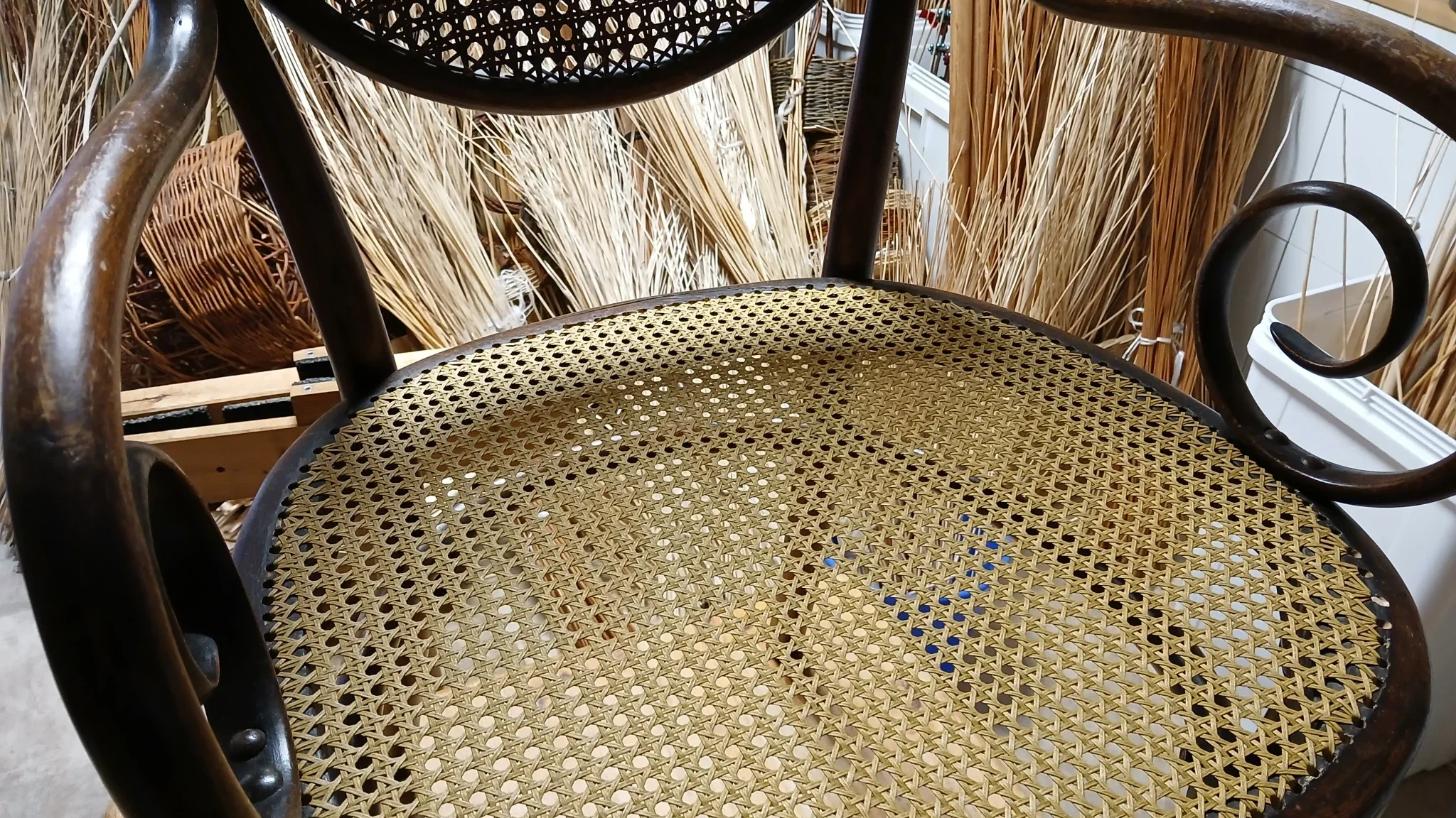 Stuhl mit dunkelbraunem Holzrahmen und Sitzfläche aus geflochtenem Rattan in Wabenmuster, Armlehnen mit geschwungenen Enden.
