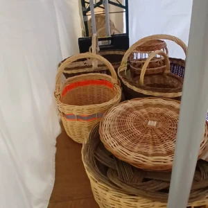 Ein Blick unter einen mit weißem Stoff verkleideten Tisch offenbart gelagerte Weidenkörbe und Korbwaren auf einem Holzfußboden.